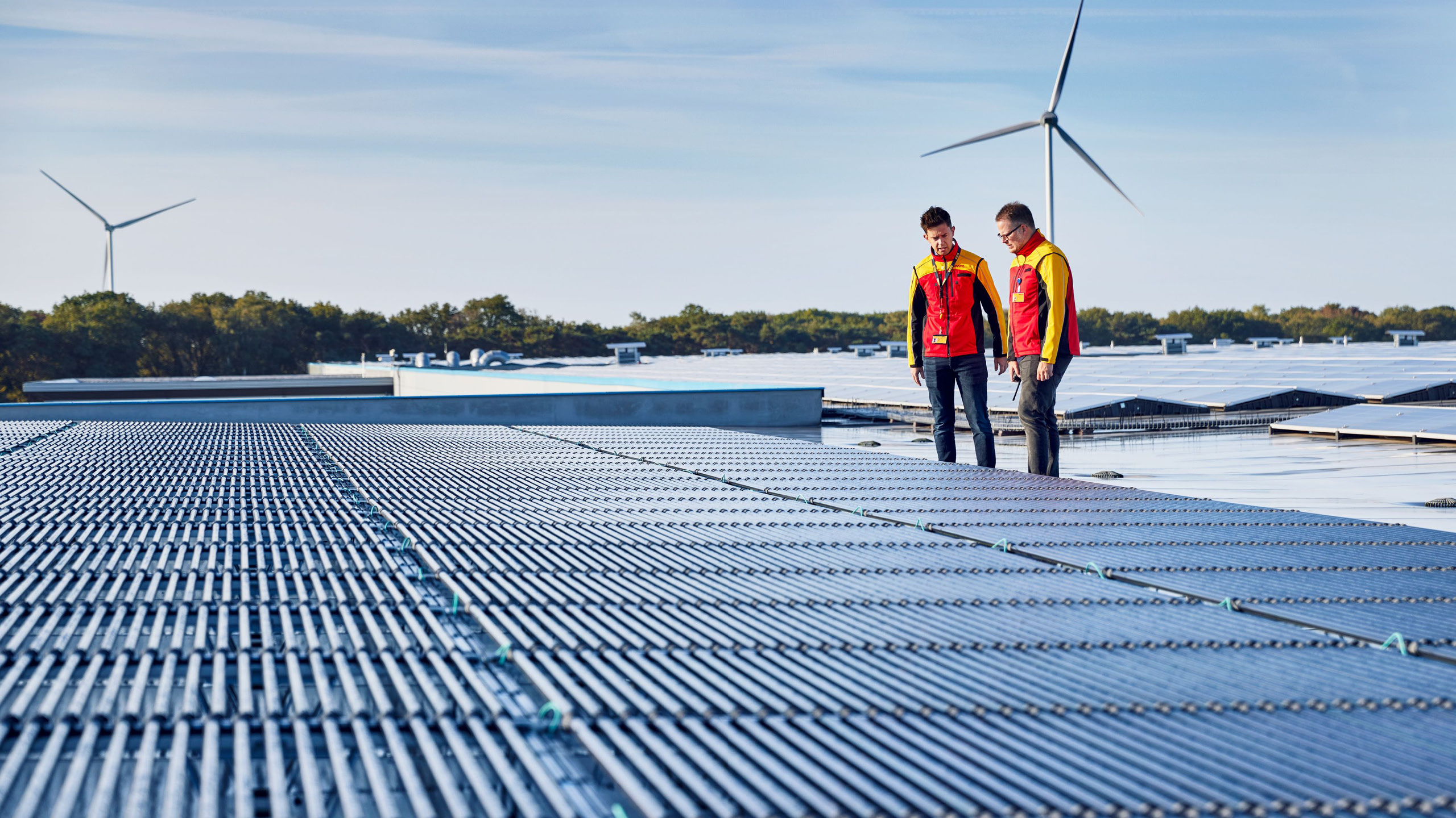 DHL-Mitarbeiter stehen zwischen Solarmodulen und Windrädern